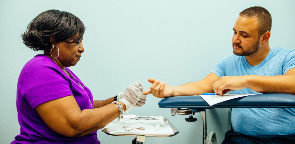 A nurse on the left pricks the finger of a patient on the right during an HIV test, while answering FAQs about HIV.