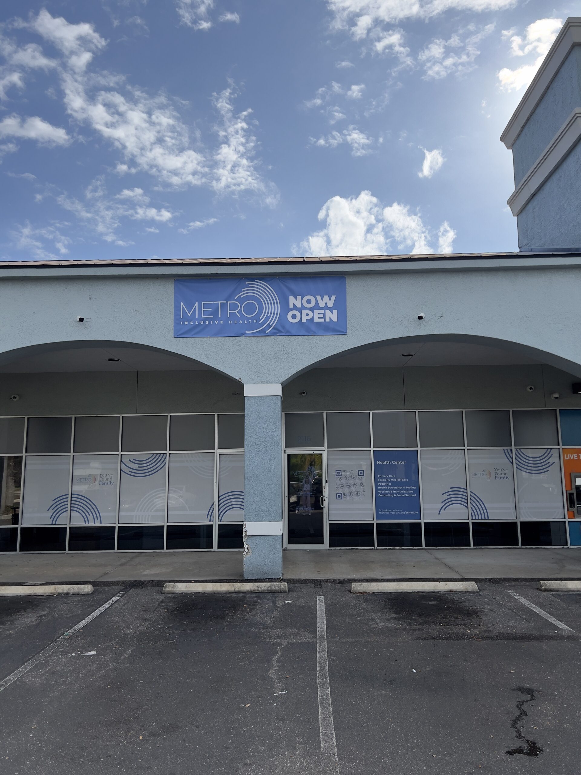 Exterior of our South St. Pete location. Blue walls and glass doors with white frosting and blue rings. Blue sign reading "METRO INCLUSIVE HEALTH NOW OPEN."