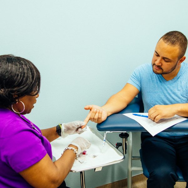 A person extends their finger for a free HIV test at Metro Inclusive Health in St. Petersburg, Florida, while learning about HIV from a specialist.